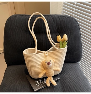 Detail of cream woven tote bag with plush bear charm and pearl button closure on a chair