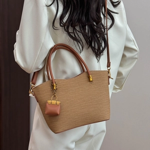 Detailed view of woven tote bag with leather straps and mini bag charm on white blazer