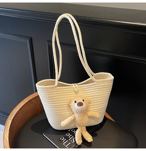 Detail of a beige woven tote bag with a plush bear charm and elegant pearl buckle