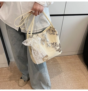 Detail of cream tote bag featuring silver sequin butterfly and lace bow with pearls