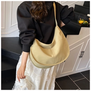 Woman wearing a large beige crescent canvas crossbody bag against a minimalist indoor stairs