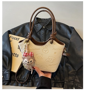 Detail of cream bucket bag with cute cartoon embossing and decorative plush charm