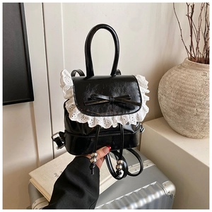 Detalle de mini mochila de charol negro con encaje blanco delicado y lazo decorativo