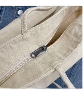 Close-up of smooth metal zipper detail on durable beige canvas tote bag with denim background