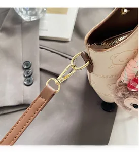Detail of high-gloss gold hardware and plush bear charm on beige printed bucket bag