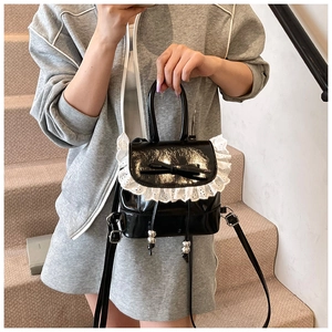 Detalle de mini mochila de charol negro con encaje y lazo en una zona de escalera