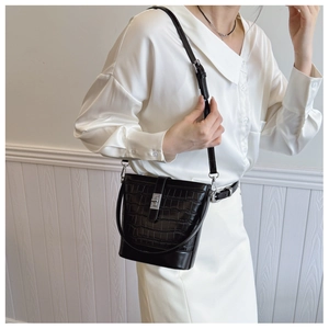 Model wearing a black crocodile embossed bucket bag with silver hardware and dual straps
