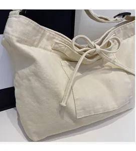 Detail of minimalist beige canvas tote featuring a bow-tie pocket and adjustable strap