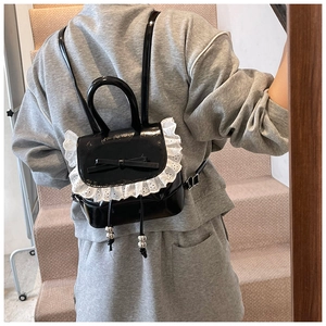 Detalle de una mini mochila de charol negro con encaje blanco y lazo llevada por una modelo