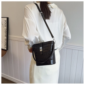 Detail of black crocodile embossed bucket bag featuring a metallic lock and long shoulder strap