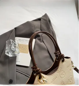 Detail of cream bucket bag showing rabbit embossed pattern and knot handle on grey suit