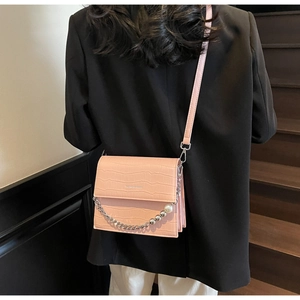 Close-up of pink croc-effect crossbody bag with silver chain and pearl pendant detail