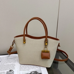 Detail of beige woven tote bag with brown leather handles and a mini bag charm accessory