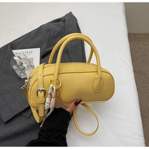 Detail of yellow lychee leather barrel bag with dual handles and woven pendant