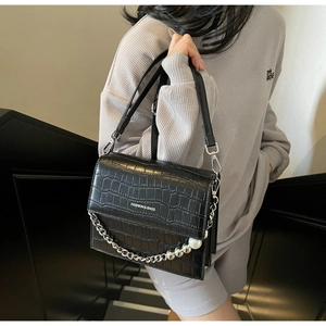 Detail of black crocodile texture handbag with silver chain and large white pearl accent