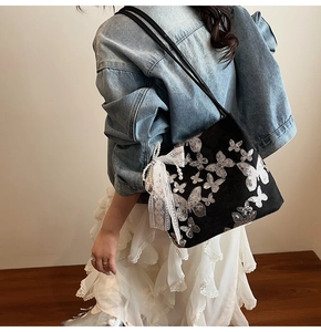 Detail of black tote bag with silver butterfly embroidery and lace bow pearl charm