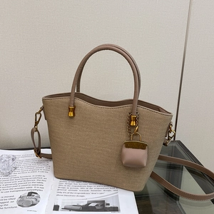 Detail of khaki woven texture tote bag with leather handle and mini purse charm