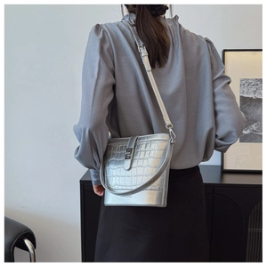 Detail view of stylish silver bucket bag with crocodile texture worn by a model