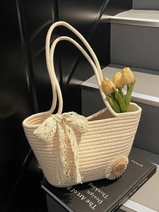 Straw tote bag with beige lace bow and sunflower accent on a designer book backdrop