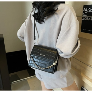 Detail of black crocodile-embossed leather bag with silver chain and white pearl handle