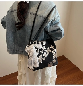 Detail of black tote bag with silver sequin butterflies and white lace bow and pearls