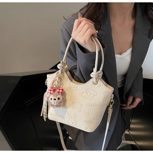 Detail of cream bucket bag with cartoon relief pattern and plush animal pendant charm