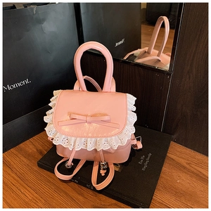 Primer plano de mini mochila rosa con encaje blanco, lazo y asa superior sobre libros