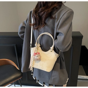 Detailed view of cream bucket bag featuring cartoon embossing and plush bear charm
