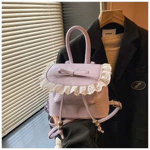 Detalle de la mini mochila lavanda con encaje blanco y lazo sobre un blazer negro