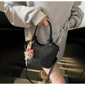 Close-up of black embossed bucket bag featuring cartoon 3D animal relief and plush charm