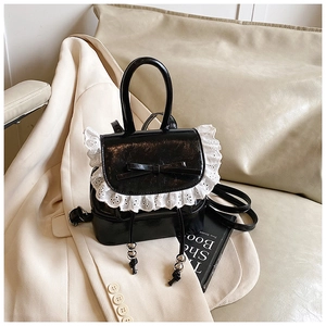 Detalle de una mini mochila negra brillante con encaje blanco y lazo decorativo