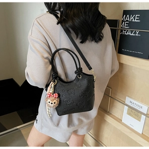 Detail of black pebbled leather bucket bag with embossed cartoon bears and plush charm