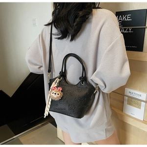 Crossbody view of black pebble leather bucket bag with bear patterns and plush charm
