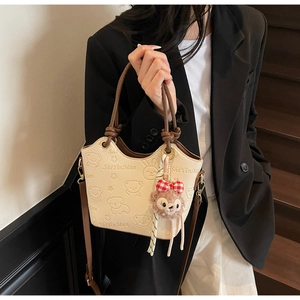 Detail shot of off-white bucket bag with cartoon embossing and a plush bear charm