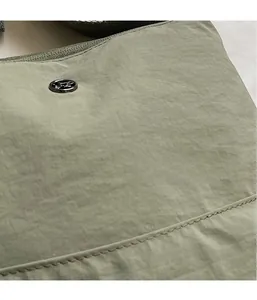Close-up of light green nylon fabric texture and circular black metal logo on a crossbody bag