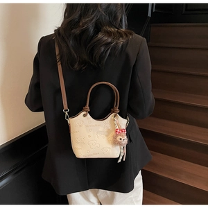 Detail of cream bucket bag with embossed animal patterns and pink plush fox pendant