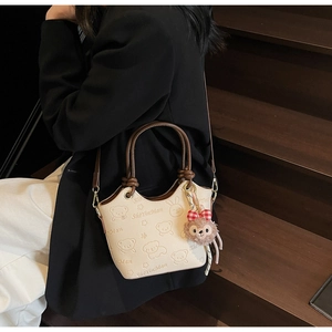 Detail of cream bucket bag with embossed cartoon bears and a plush bear pendant