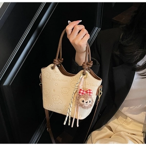 Detail of beige bucket bag featuring embossed teddy bear design and plush charm accessory