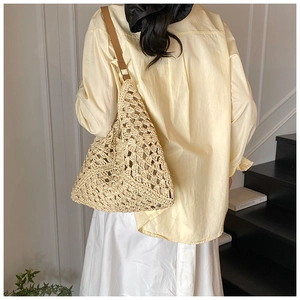 Detail of bohemian straw bag featuring hollow geometric patterns and brown leather strap