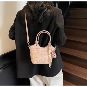 Detail of pink crossbody bucket bag with bear print and fluffy ball keychain shown on model
