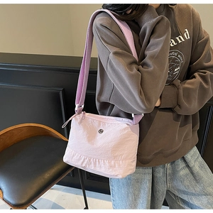 Detail view of the pink nylon crossbody bag with a purple strap and round logo decoration