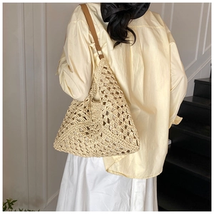 Detail of hollow woven straw shoulder bag with adjustable brown leather strap shown on model