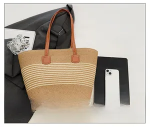 Detail of striped straw tote bag with brown leather straps on a modern desk setting