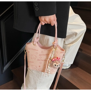 Detail of pink faux leather bucket bag with bear print and plush toy charm on stairs