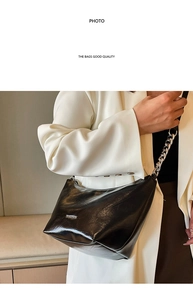Detail of black patent leather underarm bag with silver chain strap and metal logo