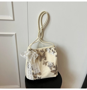 Close-up of sequined butterfly embroidery and lace pearl pendant on cream tote bag