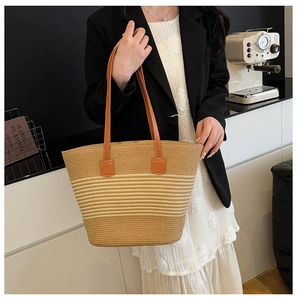 Close-up of woven straw tote bag with striped gradient design and leather handles