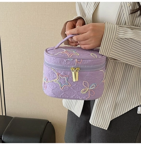 Detail der lila gesteppten Kosmetiktasche mit Sternenstickerei und goldenen Zippern