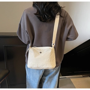 Detail of minimalist beige canvas crossbody bag showing wide strap and zip on female model