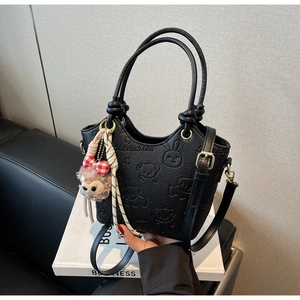 Detail of black lychee grain leather bucket bag with embossed cartoon bear and rabbit